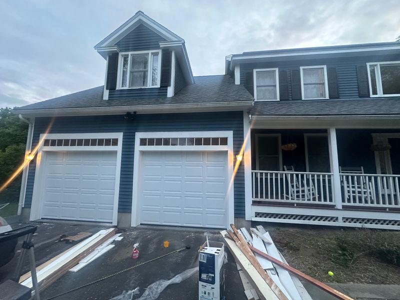 Newly installed dual white garage doors illuminated at dusk on blue colonial home in Massachusetts