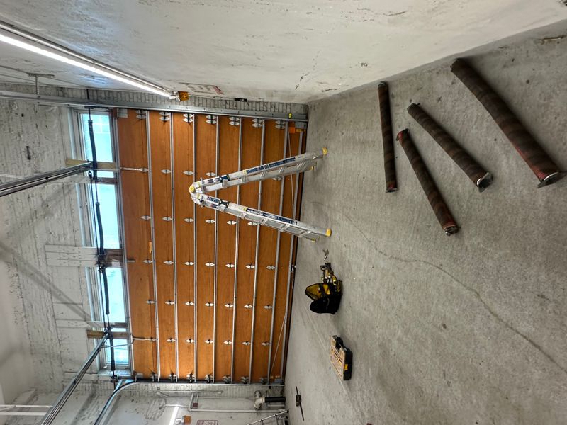Commercial wood overhead door interior being serviced with old springs visible — Massachusetts