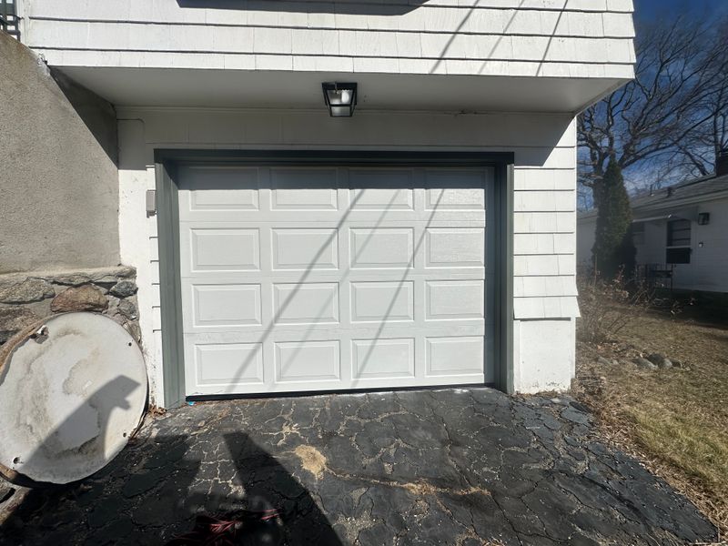 White raised-panel garage door on home with green trim and stone foundation in MA